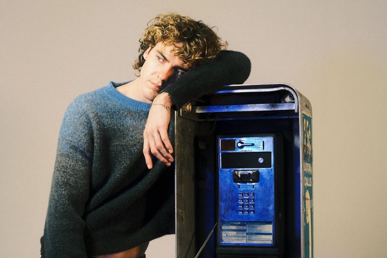 Musician Jack Gray in a blue ombre sweater leaning on a vintage blue payphone in a studio photo shoot. Photo by Grace Wethor.